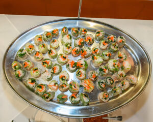 An oval tray filled with various fresh spring rolls, arranged in neat rows on a white tablecloth.