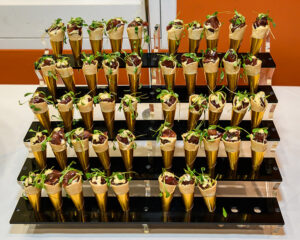 A display of mini appetizer cones filled with toppings and garnished with microgreens, arranged on a multi-tiered stand.