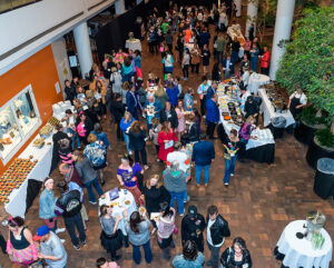 A large group of people attending an indoor party with food tables, socializing in a spacious, well-lit venue.