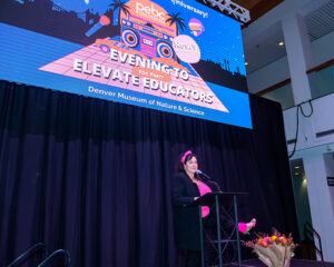 Woman speaks at podium during '80s-themed event to elevate educators at Denver Museum of Nature & Science.