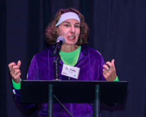 Person with a headband and name badge speaking passionately at a podium with a microphone.