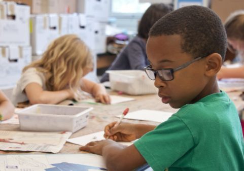 Children seated at a table in a classroom, focusing on their worksheets and activities.